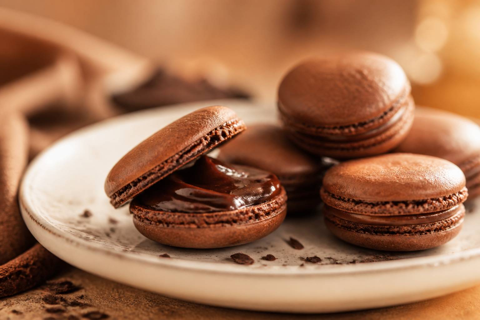Macarons au chocolat sur une assiette en céramique crème avec un macaron entrouvert à la ganache fondante